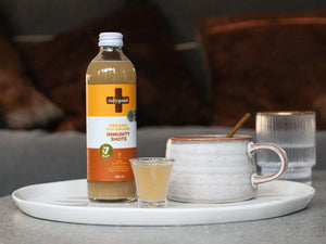 Bottle of Daily Good Ginger immunity shots alongside cup of tea 